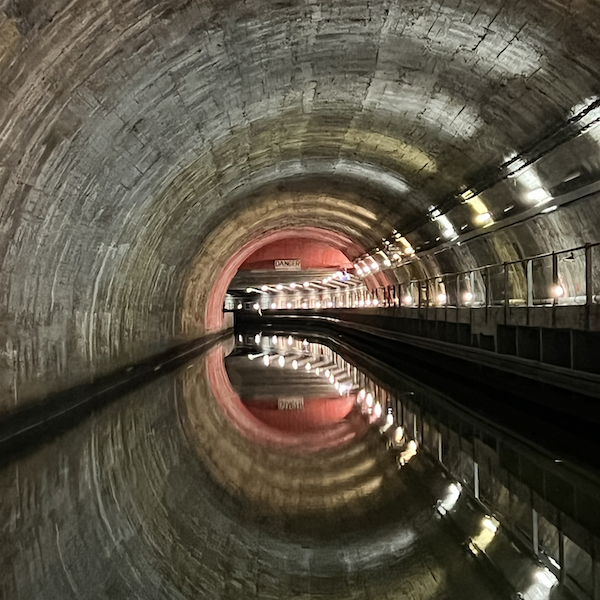 Dans un tunnel fluvial. Le reflet du plafond rond sur l'eau crée une forme de cercle. Un panneau Danger
